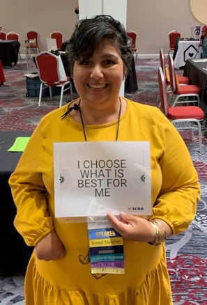 Sylvia Delgado smiling, wearing a yellow dress holding a sign that reads: "I choose what is best for me."