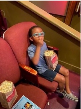 Young boy sitting in a movie theater seat eating popcorn.