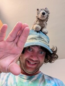 Jonathan smiling and wearing a cap with a stuffed animal.