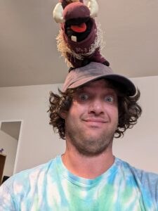 Jonathan smiling and wearing a cap with a stuffed animal.